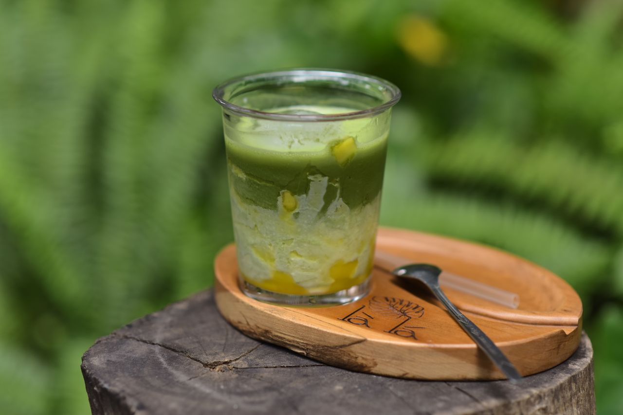 A delicious matcha and mango dessert in a clear cup outside. Perfect for summer.