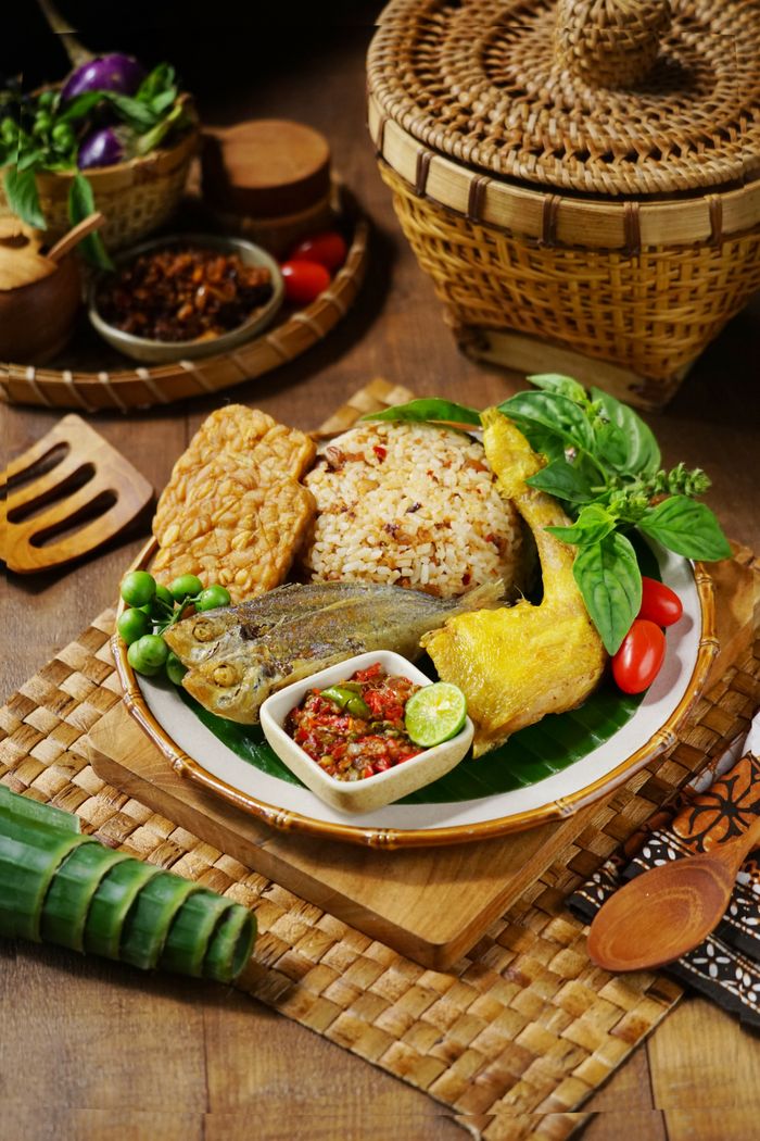 Home Authentic Nasi Liwet served with tempeh, fish, sambal, and fresh vegetables. A taste of Indonesian culture.