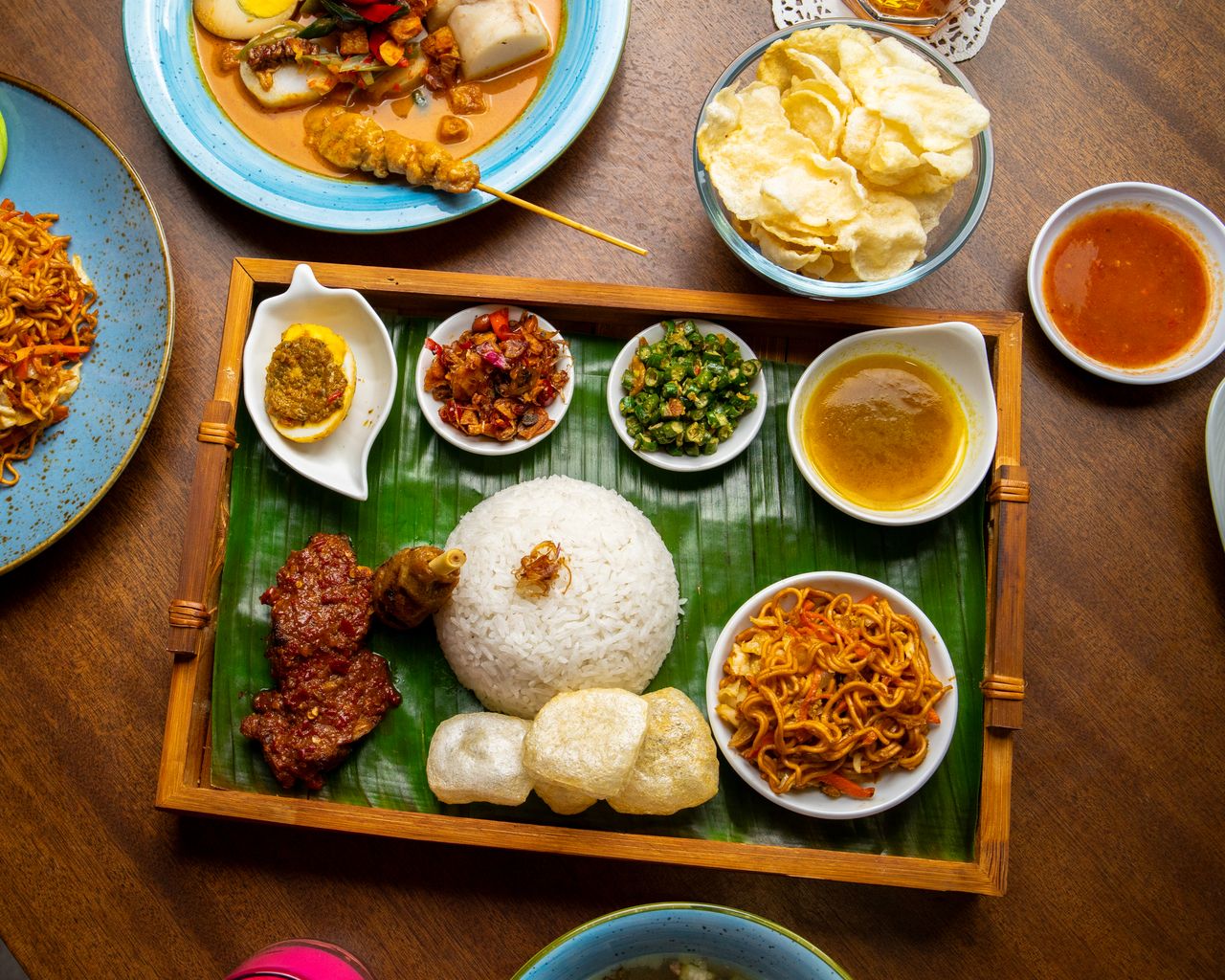Home Delicious Nasi Padang platter with rice, meat, vegetables, and crackers on a banana leaf.