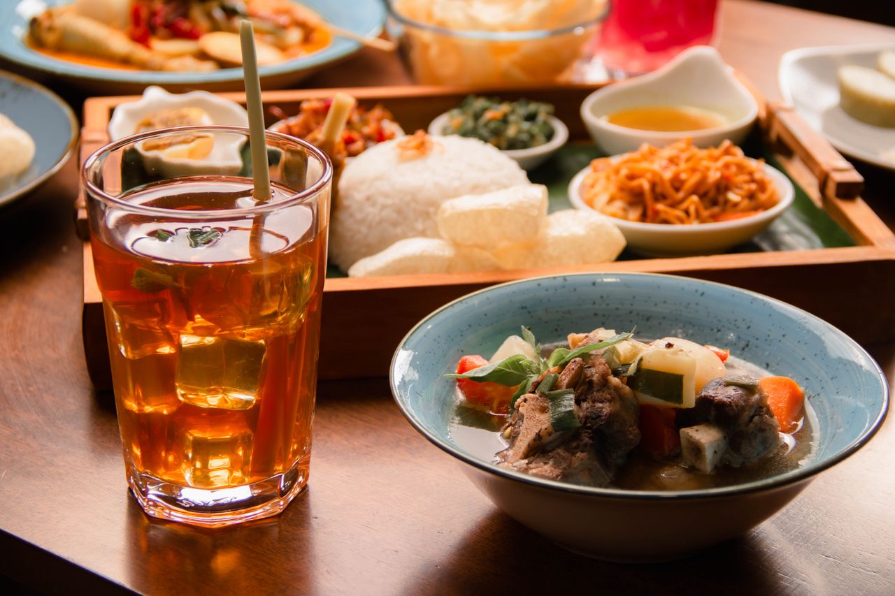 A vibrant spread of Indonesian dishes with a refreshing herbal drink served on a wooden table.