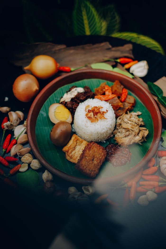 Home A delicious plate of Indonesian Nasi Campur served with rice, eggs, tempeh, and sambal, surrounded by fresh spices.